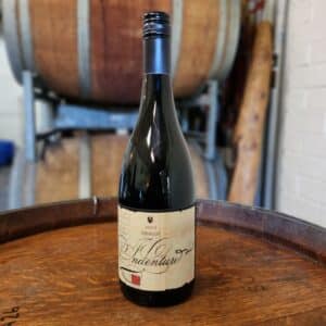 2022 Indenture Merlot Premium Red Wine, hand crafted by Rob Wilce at Innercity Winemakers, Newcastle NSW. Bottle presented on top of oak barrel with oak casks in the background.